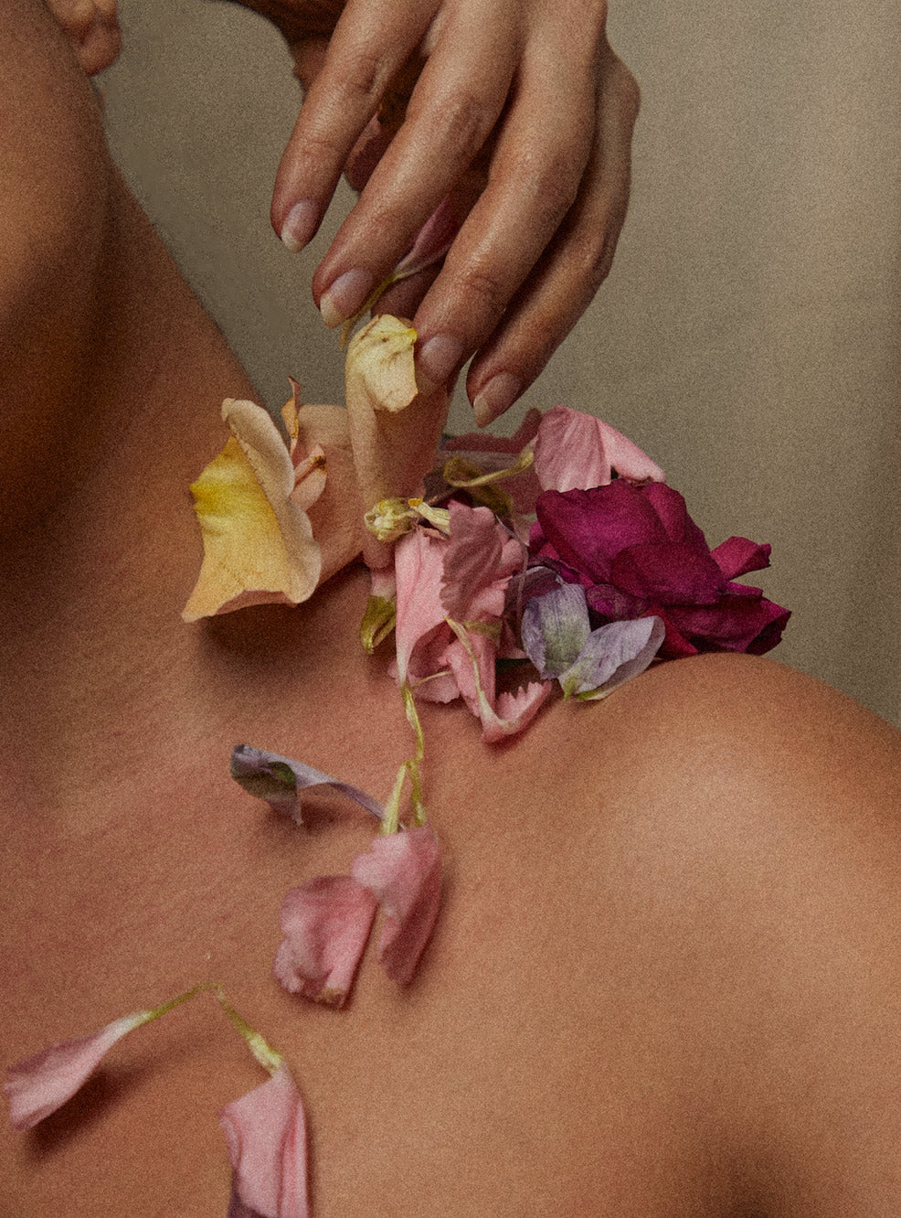 Main déposant des pétales de fleurs séchées sur une épaule nue