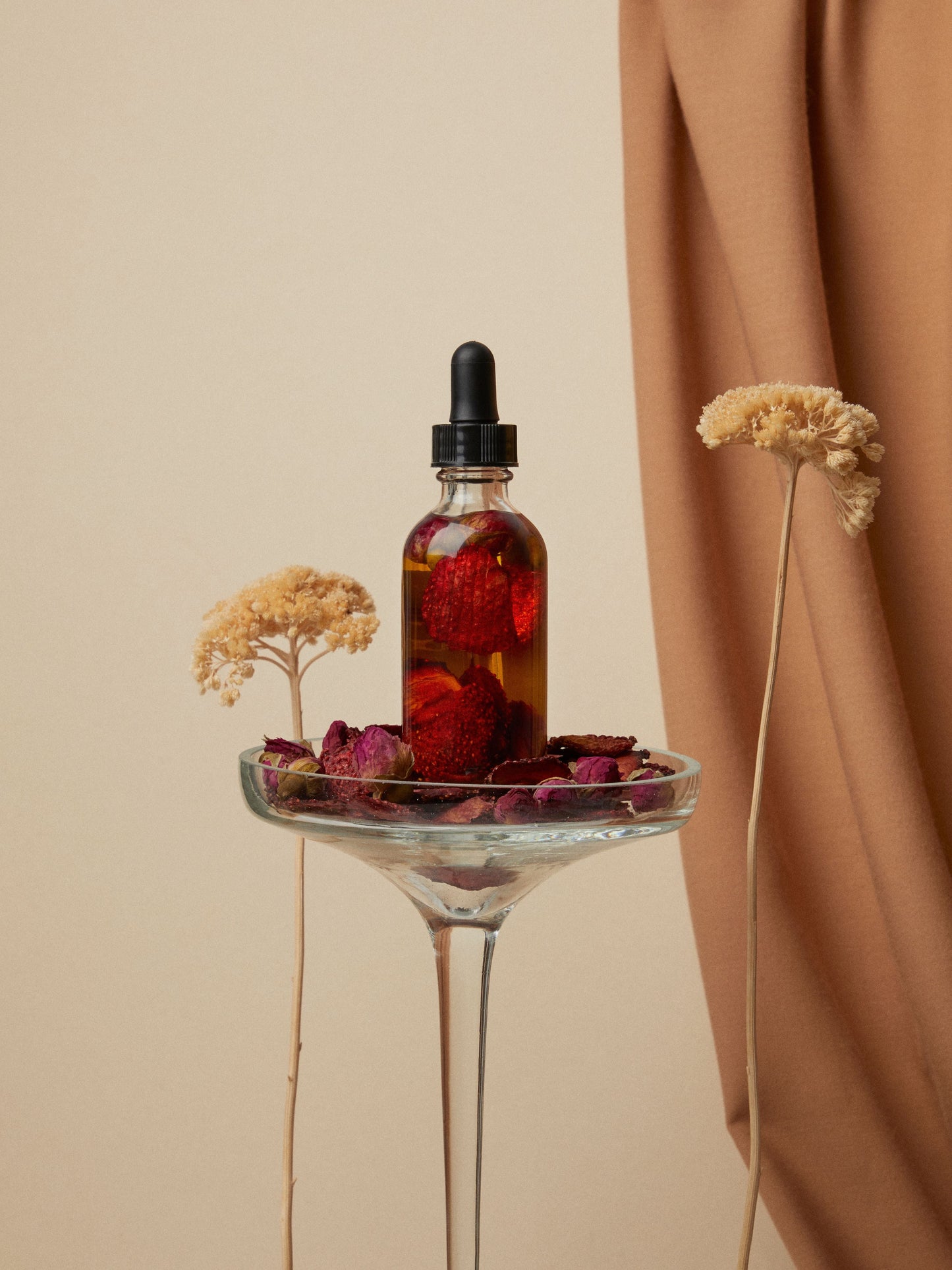 Flacon d'huile botanique infusée de pétales, posé sur une coupe de verre