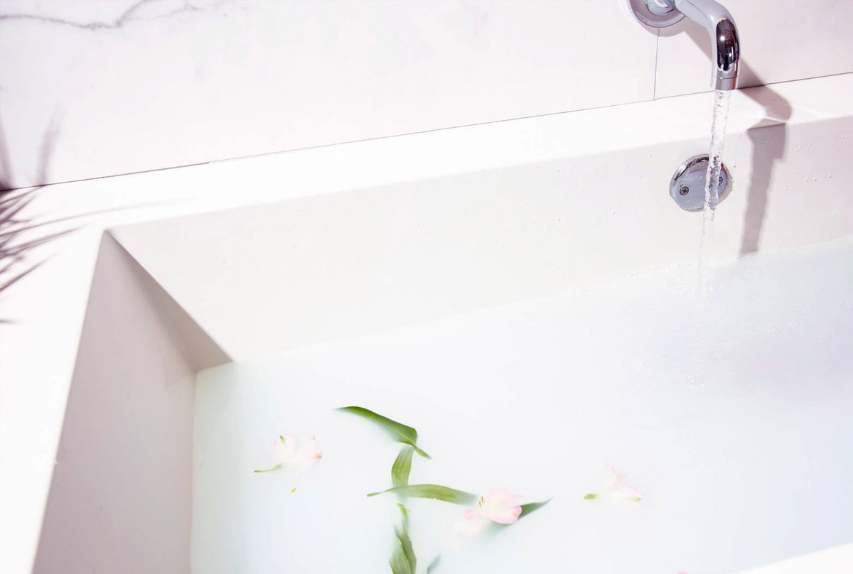 Baignoire blanche remplie d'une eau laiteuse où flottent des fleurs