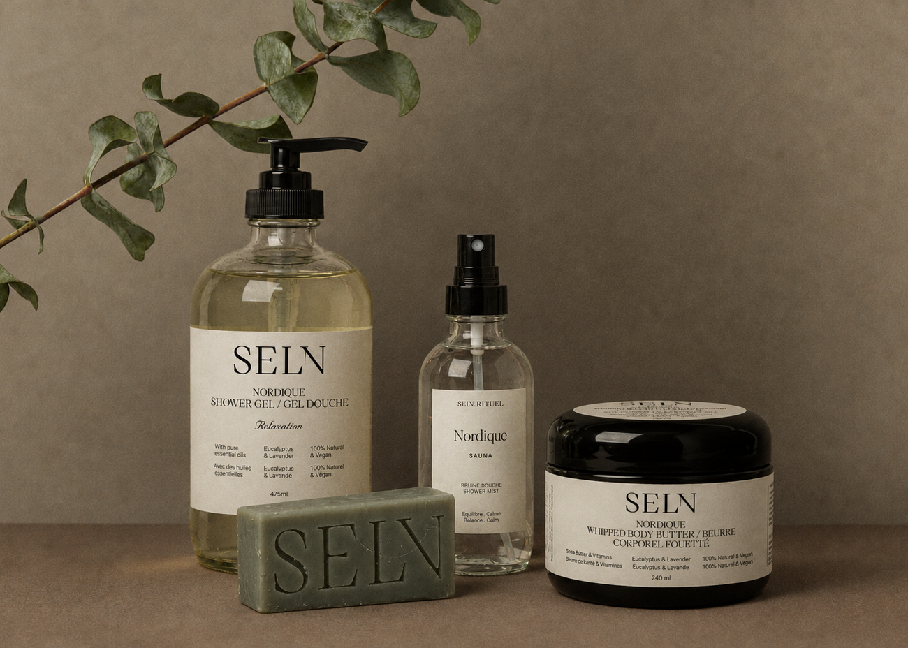 Bruines de douche Nordique Selv Rituel en flacons de verre, leurs boîtes blanches et des fleurs blanches sur un fond gris