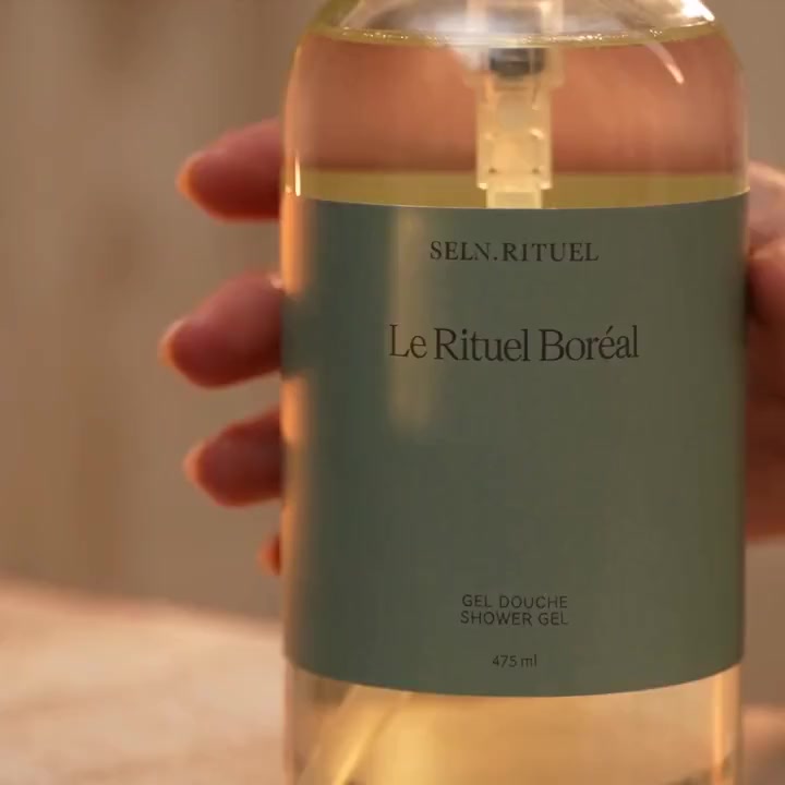 Flacon de gel douche Le Rituel Boréal Selv Rituel tenu à la main devant une chandelle, lumière chaude