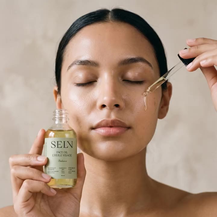 Femme aux yeux fermés qui tient le flacon d'Huile visage Selv Rituel, une goutte d'huile tombe du compte-gouttes sur sa joue
